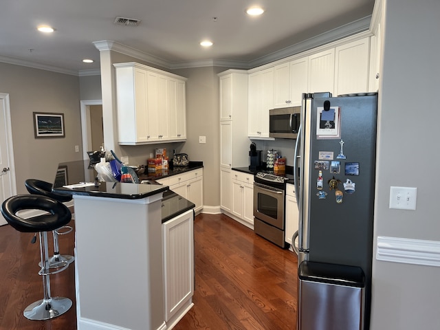 kitchen featuring a breakfast bar, dark wood-type flooring, white cabinets, appliances with stainless steel finishes, and crown molding