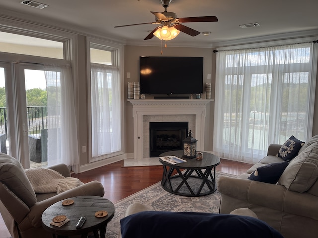 living room featuring ceiling fan, hardwood / wood-style flooring, a premium fireplace, and crown molding