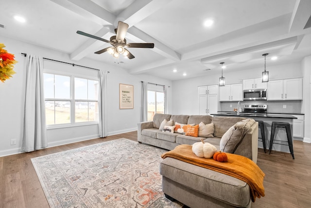 living room featuring light hardwood / wood-style flooring, ceiling fan, beamed ceiling, and sink