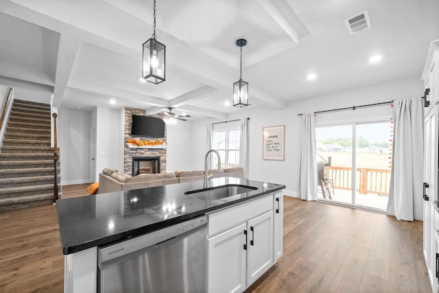 kitchen featuring sink, white cabinets, a center island with sink, a stone fireplace, and stainless steel dishwasher