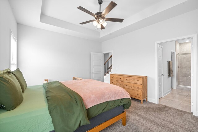 bedroom featuring ceiling fan, light colored carpet, a tray ceiling, and ensuite bath