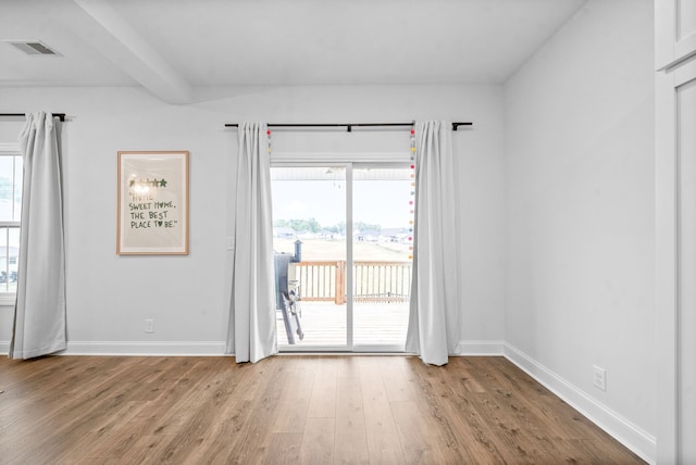 empty room with light hardwood / wood-style floors and beamed ceiling