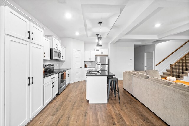 kitchen featuring appliances with stainless steel finishes, an island with sink, white cabinets, a kitchen bar, and hardwood / wood-style flooring