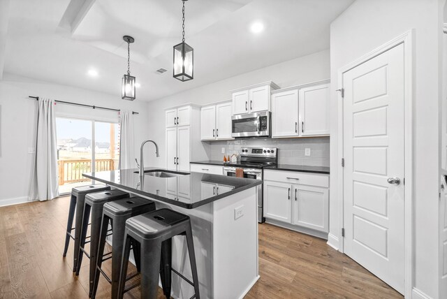 kitchen featuring appliances with stainless steel finishes, an island with sink, white cabinets, dark hardwood / wood-style flooring, and sink