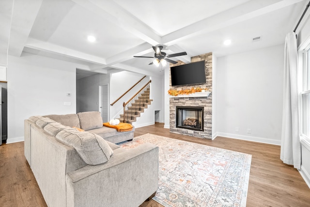 living room featuring light hardwood / wood-style floors, ceiling fan, beamed ceiling, and a fireplace