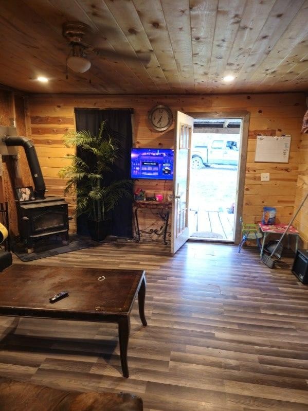 living room with wood walls, a wood stove, dark wood-type flooring, and wooden ceiling