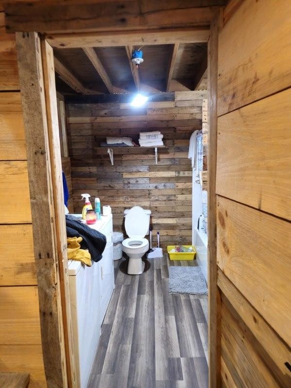 bathroom with wood walls, wood-type flooring, and toilet