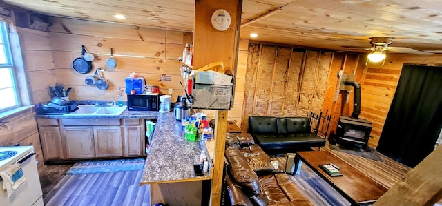 interior space featuring a wood stove, ceiling fan, sink, dark wood-type flooring, and wood walls