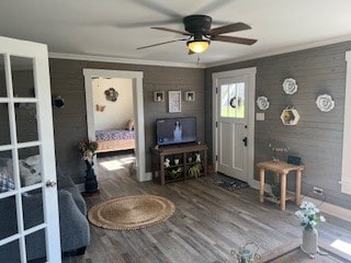 living room featuring wood-type flooring, crown molding, and ceiling fan