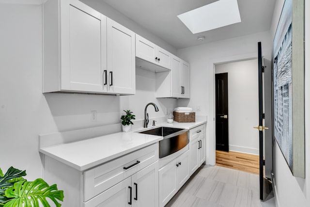 kitchen featuring a skylight, sink, and white cabinets