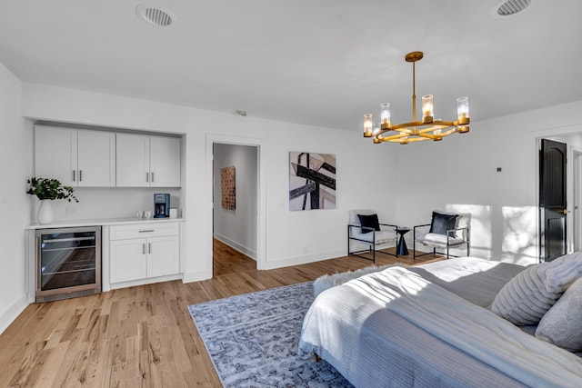 bedroom with an inviting chandelier, light hardwood / wood-style flooring, and beverage cooler