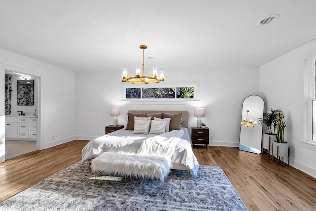 bedroom with ensuite bathroom, light wood-type flooring, and a chandelier