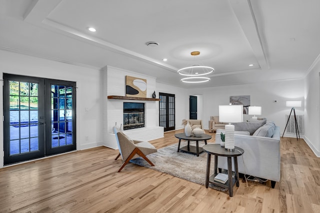 living room featuring french doors, a notable chandelier, a tray ceiling, a fireplace, and light wood-type flooring