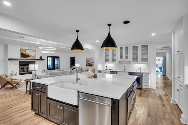 kitchen with white cabinetry, sink, hanging light fixtures, light hardwood / wood-style floors, and a kitchen island with sink