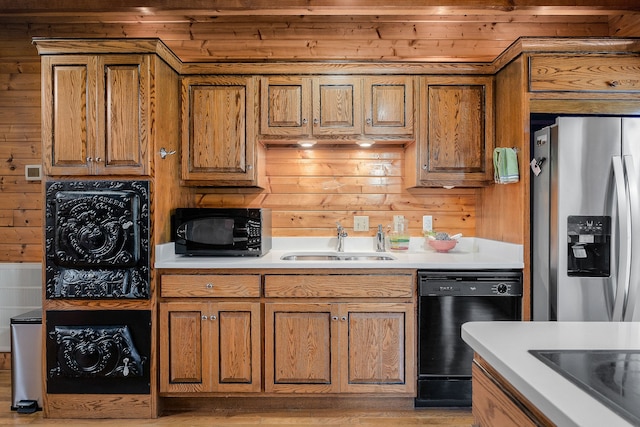 kitchen featuring light wood-type flooring, black appliances, wooden walls, and sink