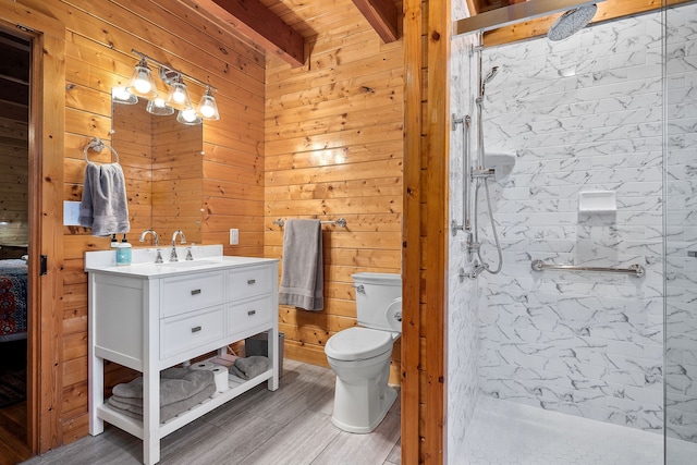 bathroom featuring a tile shower, beam ceiling, wood walls, and vanity