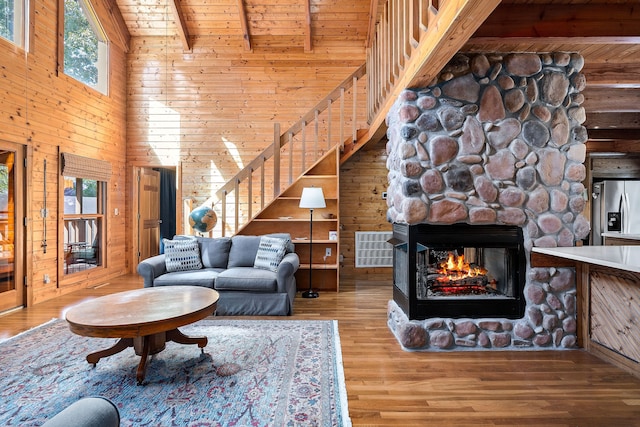 living room featuring wood ceiling, beam ceiling, a stone fireplace, wooden walls, and hardwood / wood-style flooring