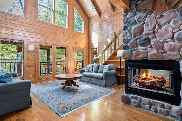 living room with beamed ceiling, wooden walls, high vaulted ceiling, a fireplace, and hardwood / wood-style floors