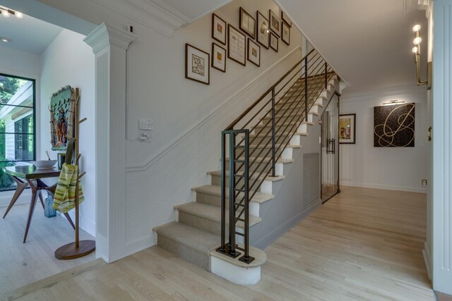 stairs featuring wood-type flooring, decorative columns, and ornamental molding