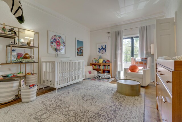 bedroom featuring a nursery area, hardwood / wood-style flooring, and crown molding