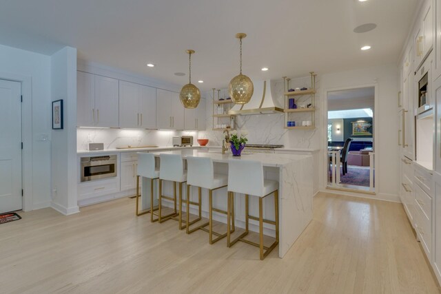 kitchen featuring pendant lighting, white cabinets, backsplash, and premium range hood