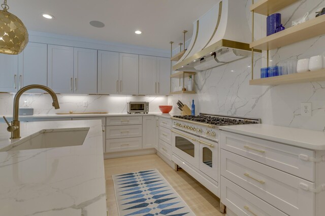 kitchen with island exhaust hood, range with two ovens, and white cabinetry