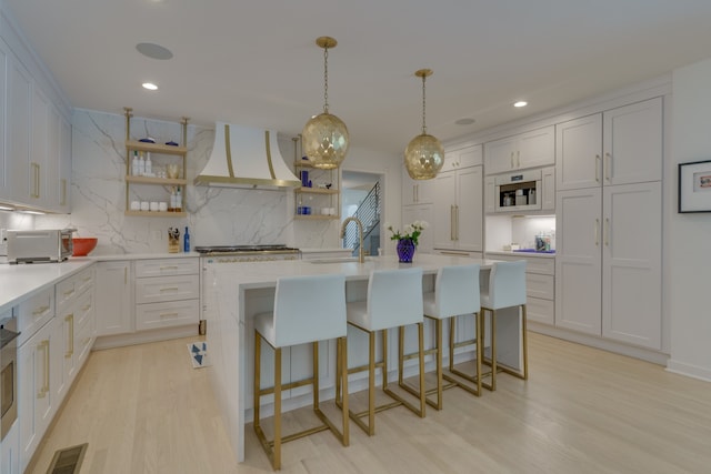 kitchen featuring an island with sink, white cabinetry, light hardwood / wood-style floors, and wall chimney range hood