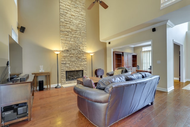 living room featuring ceiling fan, ornamental molding, wood-type flooring, a stone fireplace, and a towering ceiling