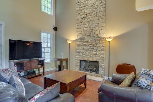 living room with wood-type flooring, a high ceiling, a wealth of natural light, and a stone fireplace