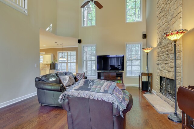 living room with ceiling fan, hardwood / wood-style flooring, a high ceiling, a fireplace, and crown molding