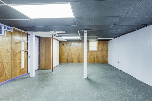 basement featuring a drop ceiling and wooden walls