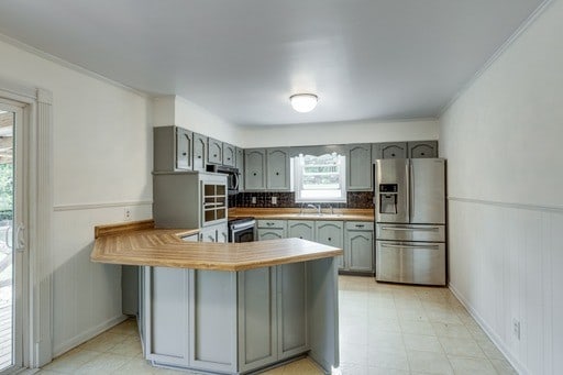 kitchen featuring ornamental molding, kitchen peninsula, backsplash, gray cabinets, and stainless steel appliances