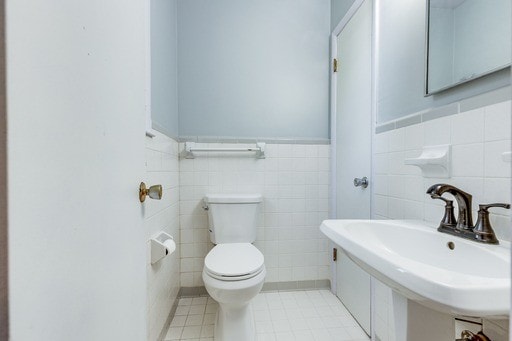 bathroom with tile walls, tile patterned flooring, toilet, and sink