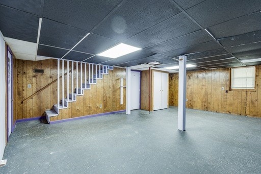 basement featuring a drop ceiling and wooden walls