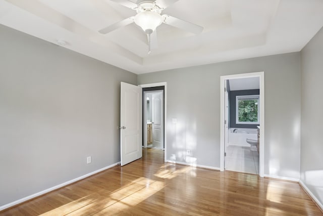 unfurnished bedroom with a raised ceiling, hardwood / wood-style floors, and ensuite bath