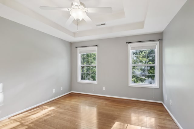 spare room with a tray ceiling, light hardwood / wood-style floors, and ceiling fan