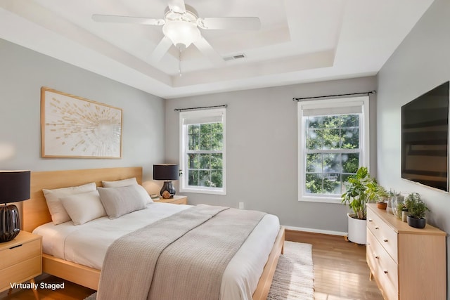 bedroom with ceiling fan, wood-type flooring, and a raised ceiling