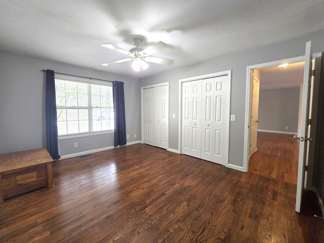 unfurnished bedroom featuring ceiling fan, two closets, and dark hardwood / wood-style floors