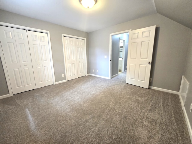 unfurnished bedroom featuring dark carpet, two closets, and vaulted ceiling