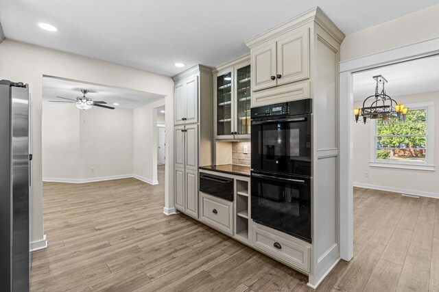 kitchen with light hardwood / wood-style flooring, black double oven, cream cabinetry, and stainless steel refrigerator