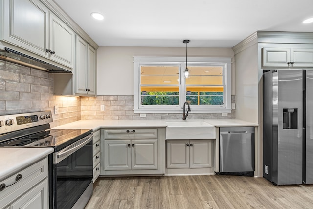 kitchen with decorative backsplash, hanging light fixtures, sink, appliances with stainless steel finishes, and light hardwood / wood-style floors