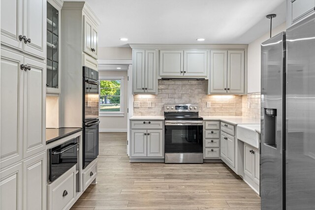 kitchen featuring backsplash, appliances with stainless steel finishes, decorative light fixtures, and light wood-type flooring