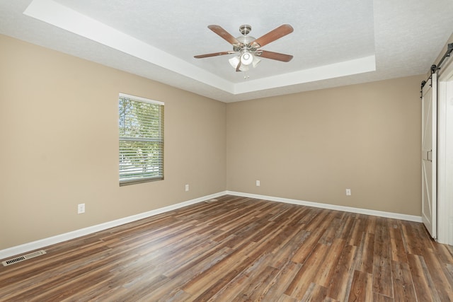 spare room featuring ceiling fan, a raised ceiling, a textured ceiling, a barn door, and dark hardwood / wood-style floors