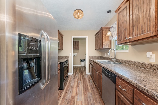 kitchen featuring appliances with stainless steel finishes, sink, light wood-type flooring, a textured ceiling, and hanging light fixtures