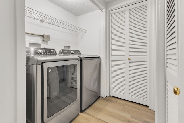 laundry area featuring a textured ceiling, washing machine and dryer, and light hardwood / wood-style floors