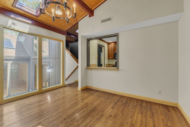 empty room featuring lofted ceiling with skylight, a chandelier, light hardwood / wood-style flooring, and wooden ceiling