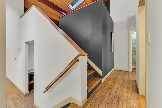 stairs featuring a high ceiling, wood ceiling, hardwood / wood-style flooring, and a skylight