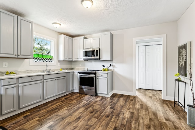 kitchen featuring sink, a textured ceiling, dark wood-type flooring, gray cabinets, and appliances with stainless steel finishes