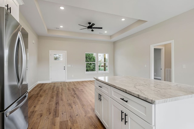 kitchen with light wood-type flooring, stainless steel refrigerator, light stone countertops, white cabinets, and a tray ceiling