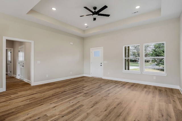 unfurnished living room with light hardwood / wood-style flooring, ceiling fan, and a raised ceiling